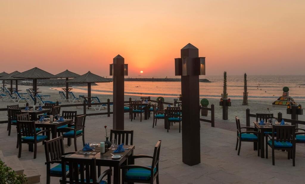 Beachfront dining terrace at sunset beside the Arabian Gulf